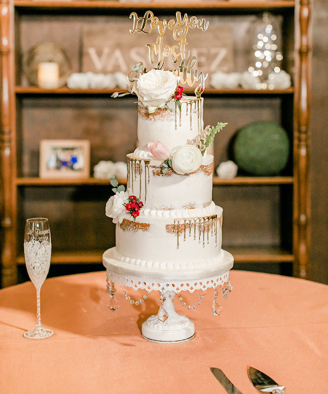 A three-tiered naked cake with gold icing and custom cake topper. 