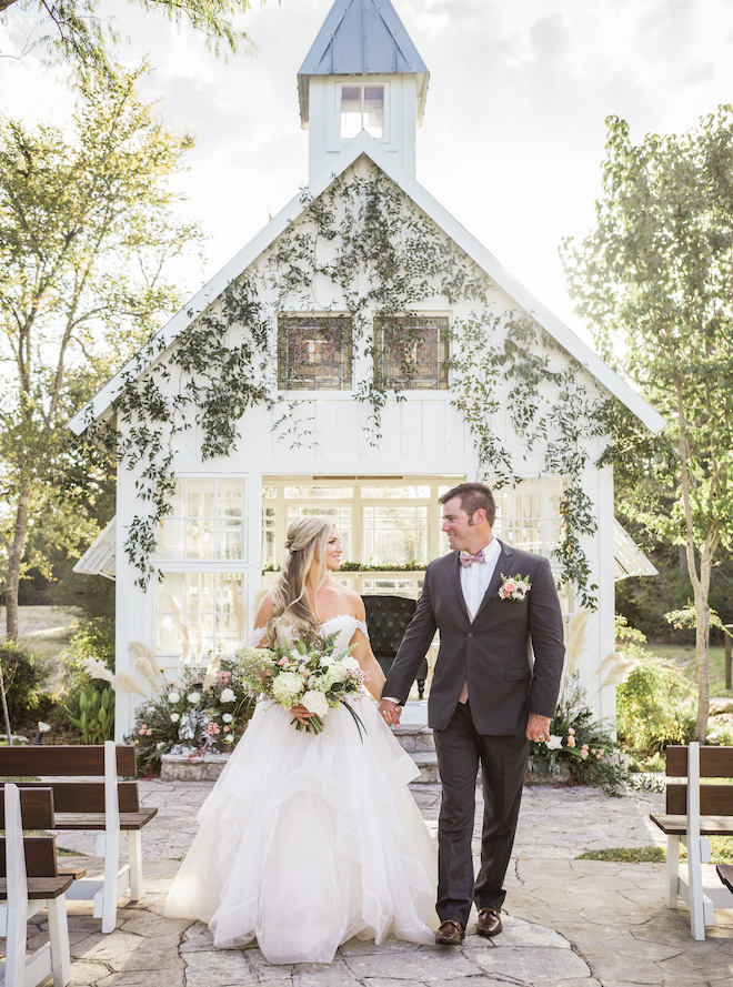 Woman wearing wedding dress and a man in a suit holding hands outside the 7F Lodge & Events chapel.