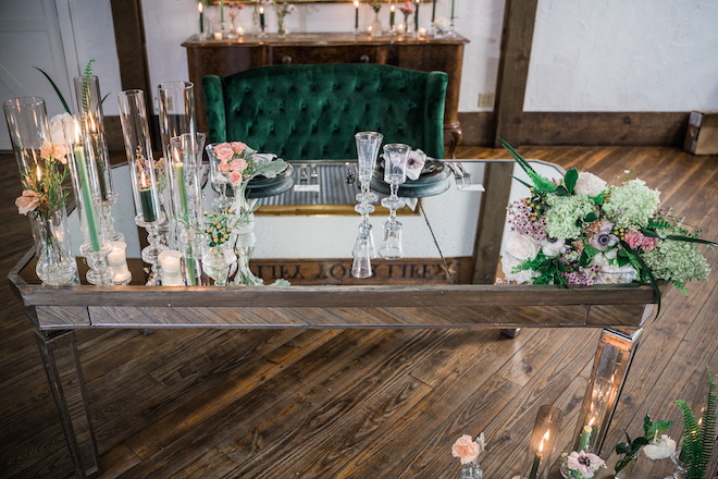 Velvet green loveseat and the couples table at the reception filled with flowers and candles.