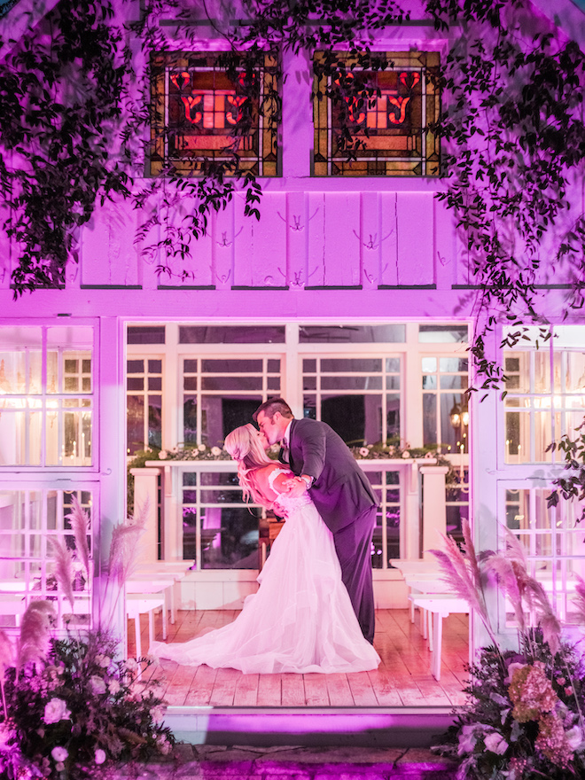The bride and groom kissing in the lit-up chapel.