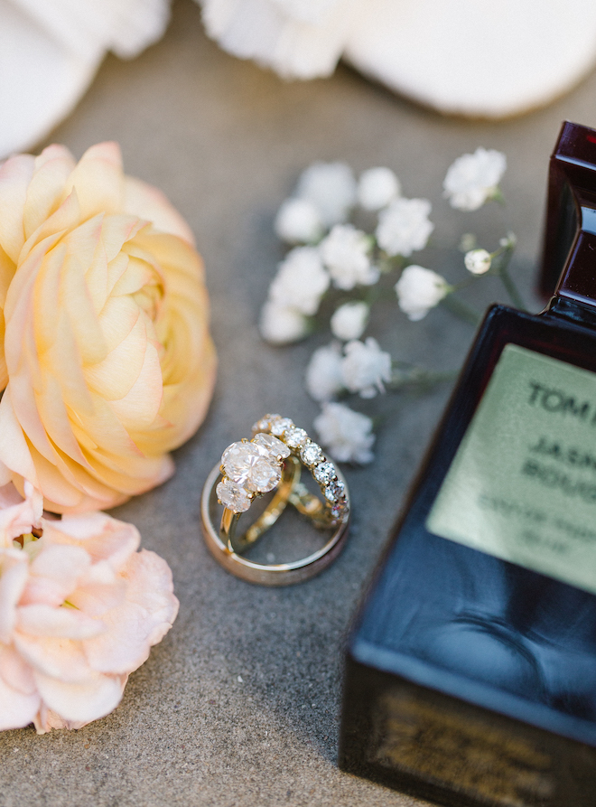 The bride's rings laying with flowers and a Tom Ford perfume bottle. 