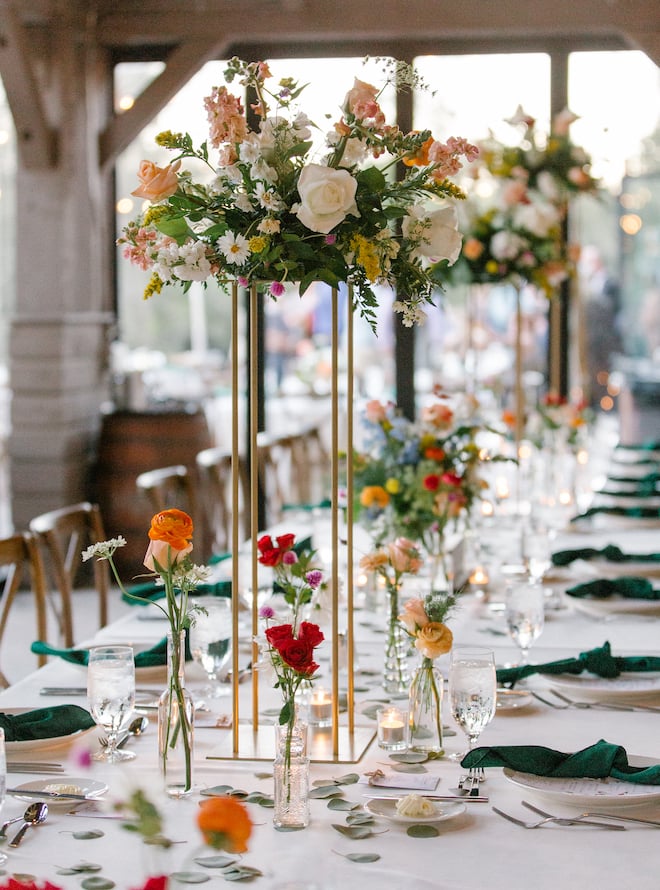 The centerpiece of the long reception table with delicate red, orange, pink and yellow flowers. 