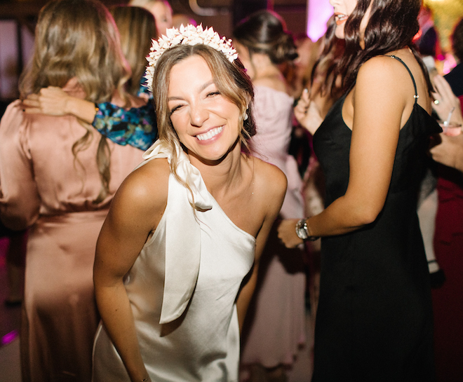 The bride smiling in her short satin dress on the dance floor. 