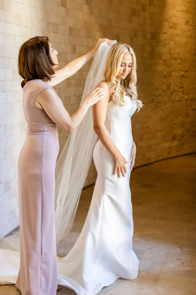 A woman helping the bride put on the veil before her tropical wedding.
