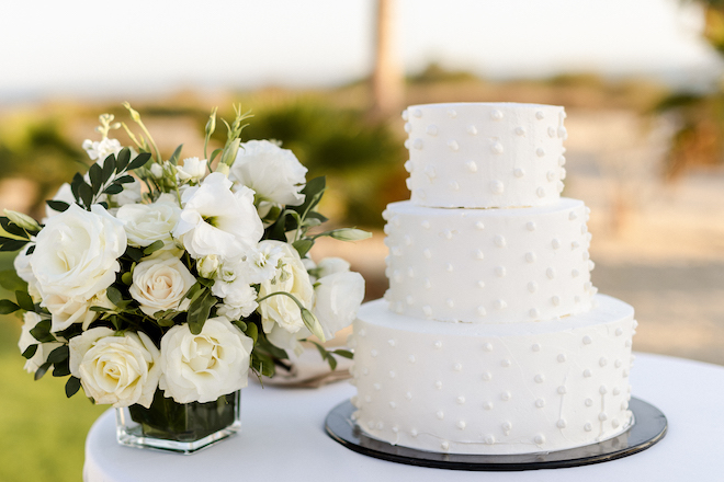 The three tier white dotted wedding cake sitting next to a bouquet of white flowers.