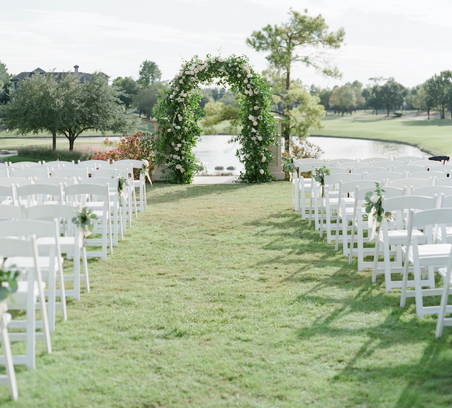 A ceremony setup at Houston venue, Royal Oaks Country Club, with a floral installation overlooking a pond and golf course. 