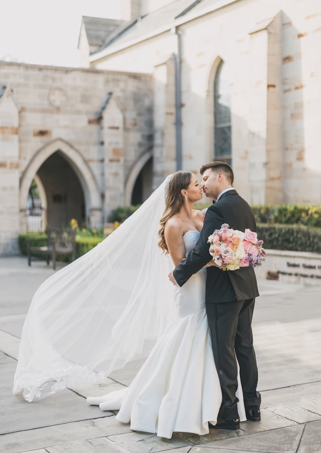 The bride and groom kissing outside the church with the bride's veil flowing in the wind.