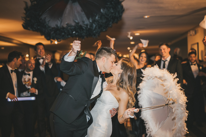 The bride and groom kissing with feathered umbrellas at their glam ballroom wedding.