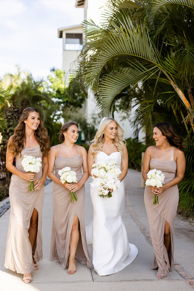 The bride and her bridesmaids in taupe gowns walking with their white bouquets.