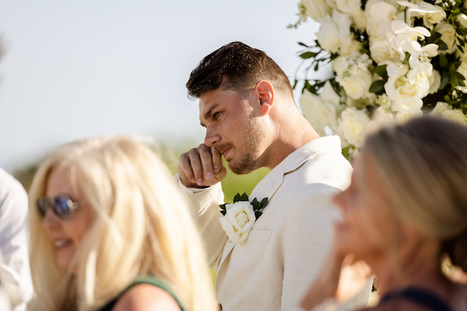 The groom wiping a tear as he watches the bride walking down the aisle.