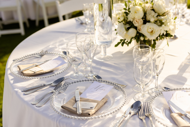 The reception table layout with taupe napkins and silver flatware, with a white bouquet centerpiece.