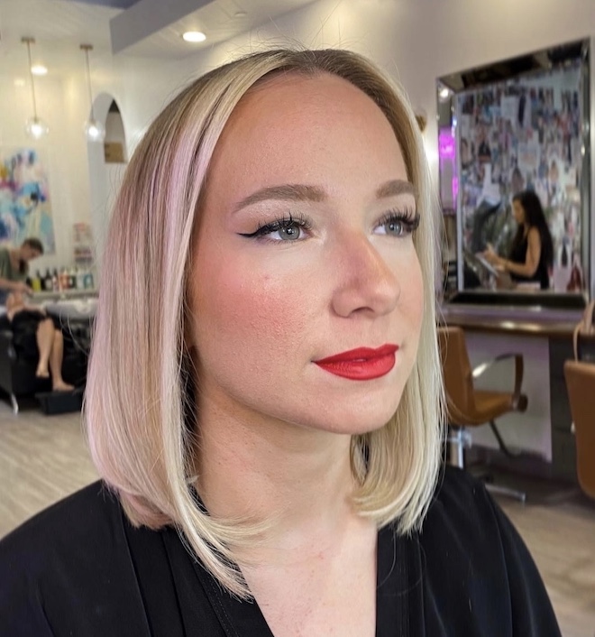 A women with red lipstick with blonde shoulder-length hair parted down the middle by hair stylist, The Beauty Lounge in Houston, Texas.
