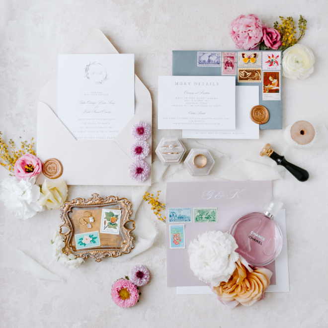 A flat lay of the wedding stationery with pastel florals laying alongside the stationery and wedding bands. 