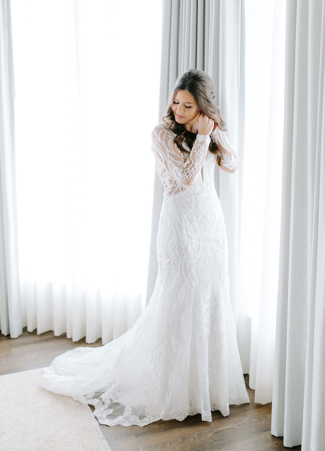 Bride putting on her earrings aside a window in the bridal suite at Brenham wedding venue, Deep in The Heart Farms. 