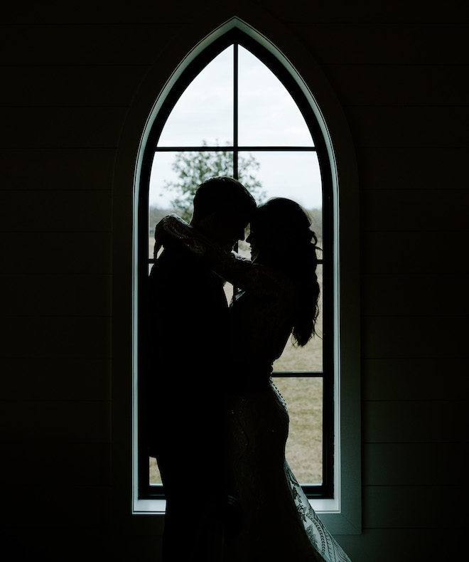 The bride and groom hugging by the window of the chapel.