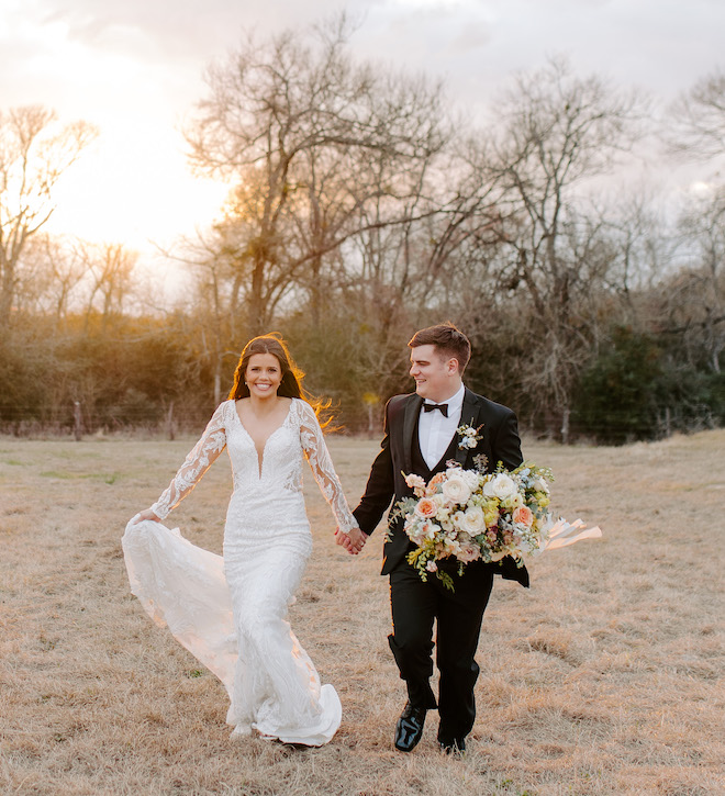 The bride and groom holding hands as they walk in the field of the Brenham venue.
