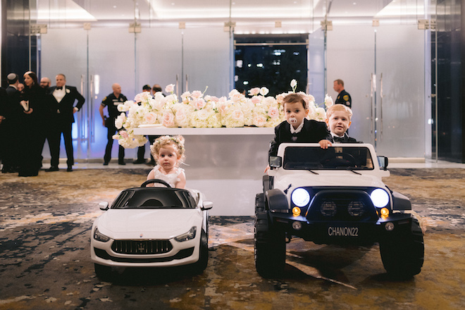 Children in formal clothing, sitting in remote powered toy cars at a wedding ceremony at the post oak hotel uptown houston.