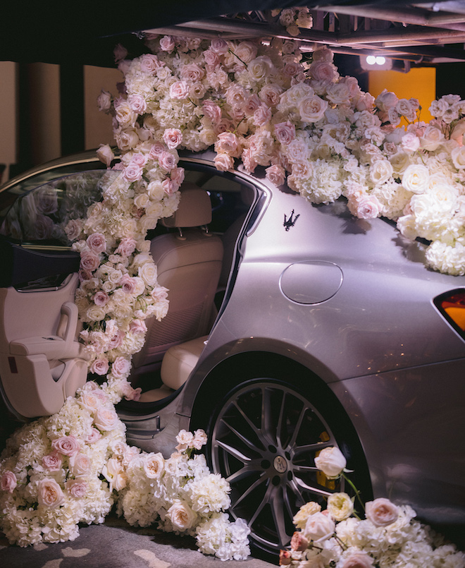A Gray Maserati covered in white, blush and ivory flowers inside a ballroom at the post oak hotel during a wedding reception.