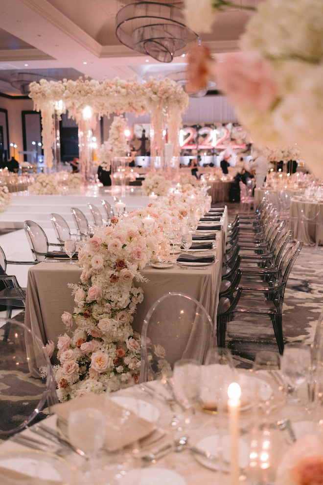 The ballroom at post oak hotel decorated for a wedding reception with blooming floral arrangements, white and pink decor and ghost chairs. 