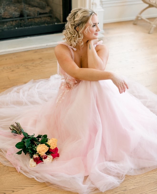 A woman in a pink gown with curly blonde short hair with a braid.