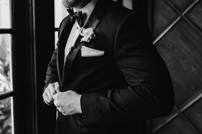 The groom buttoning his suit jacket.