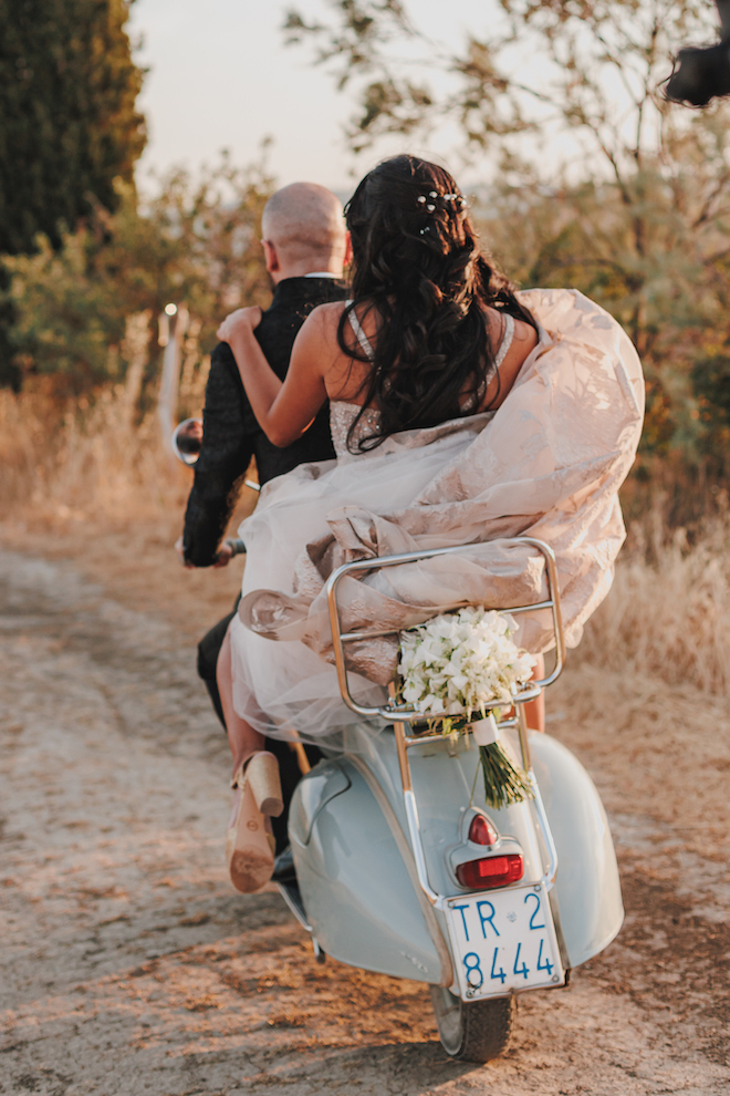 The bride and groom driving away on a Vespa after their wedding ceremony in the Tuscan countryside.