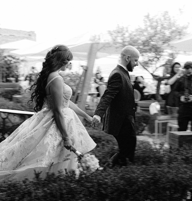 The bride and groom holding hands as they walk into their al fresco reception.