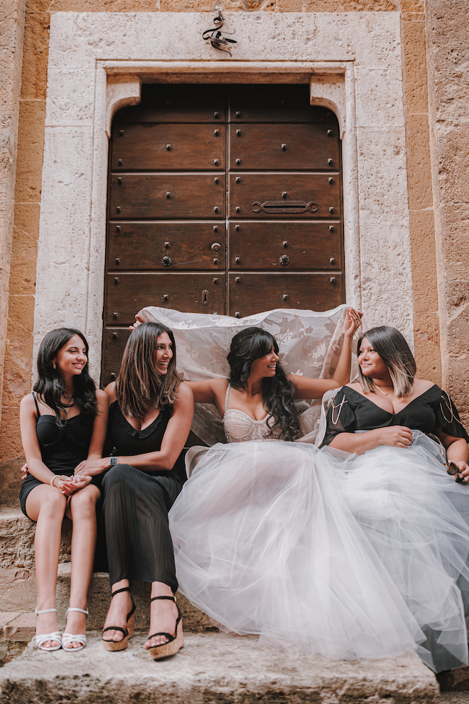 The bride holding the veil over her head while smiling with her friends.