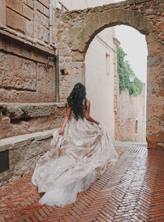 The bride holding her dress as she walks through an arch before her intimate wedding in the Tuscan countryside.