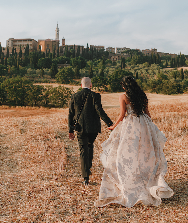 The bride and groom holding hands as they walk through the Tuscan countryside.