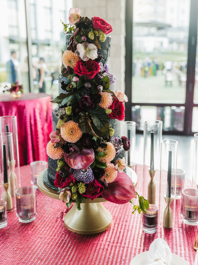 A four-tier black cake decorated with jewel toned florals.