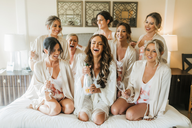 The bride holding a bottle of champagne laughing with her bridesmaids.