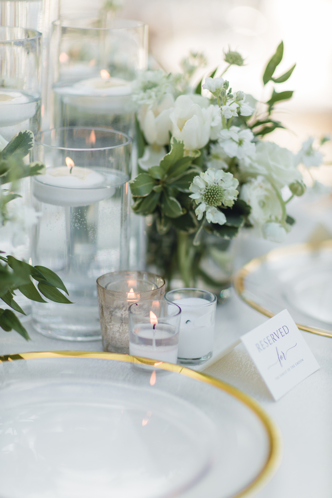 Candles, white flowers and glass plates with a gold rim and a "reserved" card on a table.