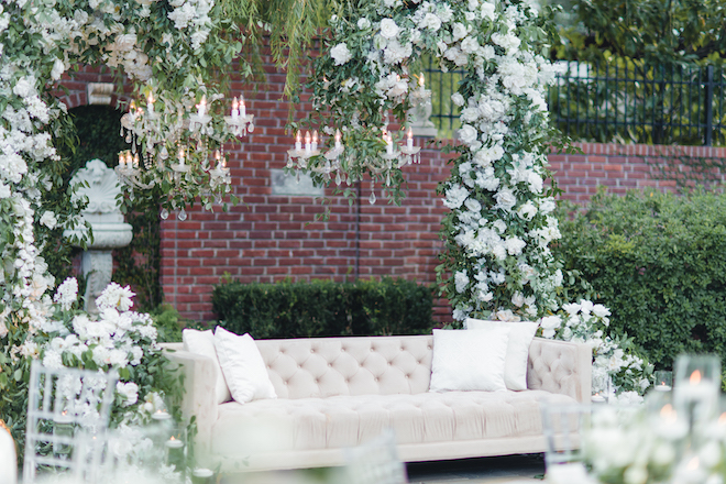 A white couch underneath greenery and white flowers for the garden Nikkah. 