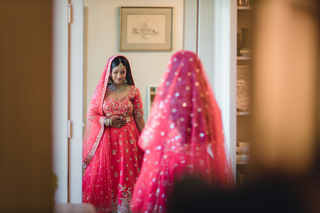 The bride looking down and smiling as she stands in front of a mirror.