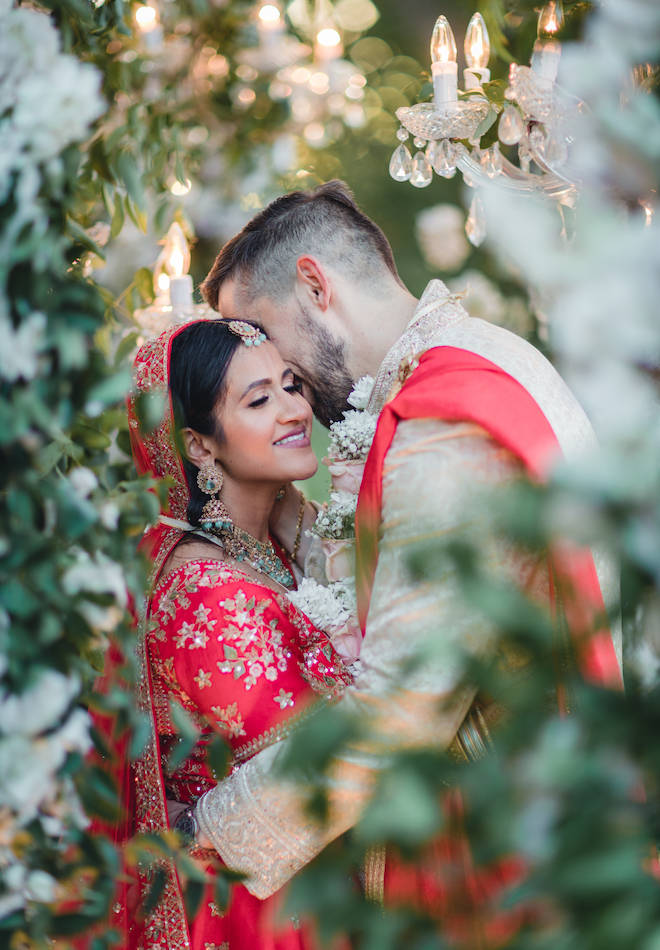 The bride and groom hugging surrounded by chandeliers and greenery.