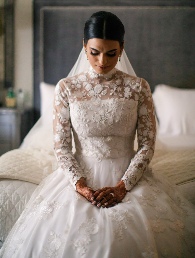 The bride sitting in her wedding gown on her parent's bed.