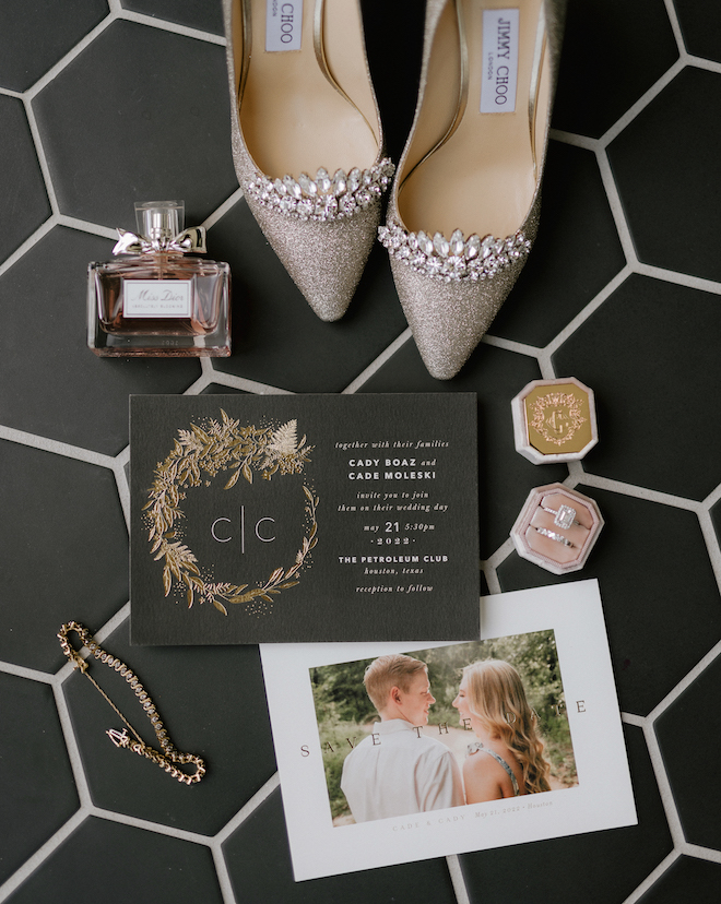 Pair of jimmy choo heels, Miss Dior perfume, a wedding invitation, Save the date and a wedding ring sit on the tiled bathroom floor of C. Baldwin Hotel