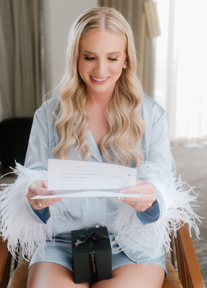 A blonde bride reads a letter from the groom on her wedding day at C. Baldwin Hotel Houston.