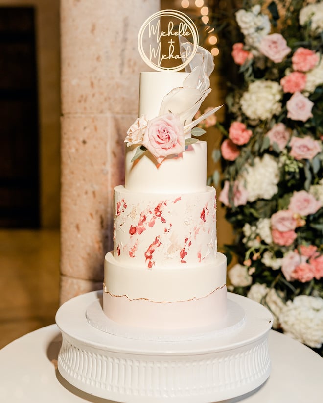A four-tiered white wedding cake with different shades of pink.