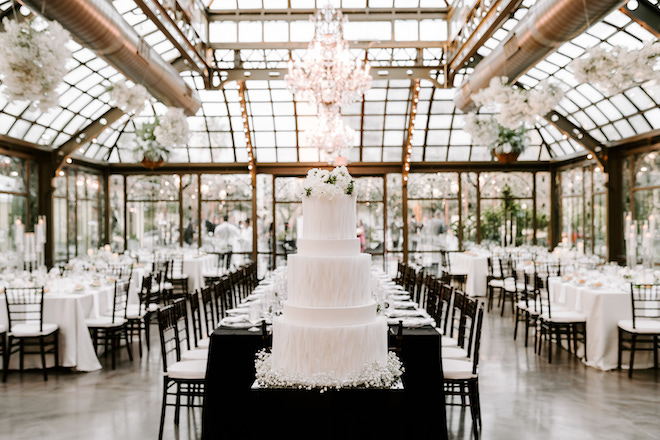 A grand white cake in front of the reception space for the winter wedding in Galveston, Texas.