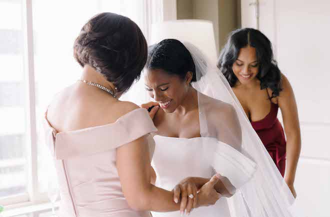 The bride and her mother holding each other's arms and smiling as they look down.