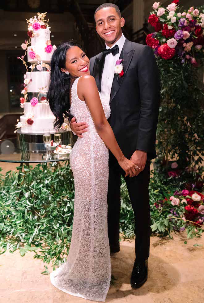 The bride and groom smiling in front of the cake at their luxurious Houston wedding.