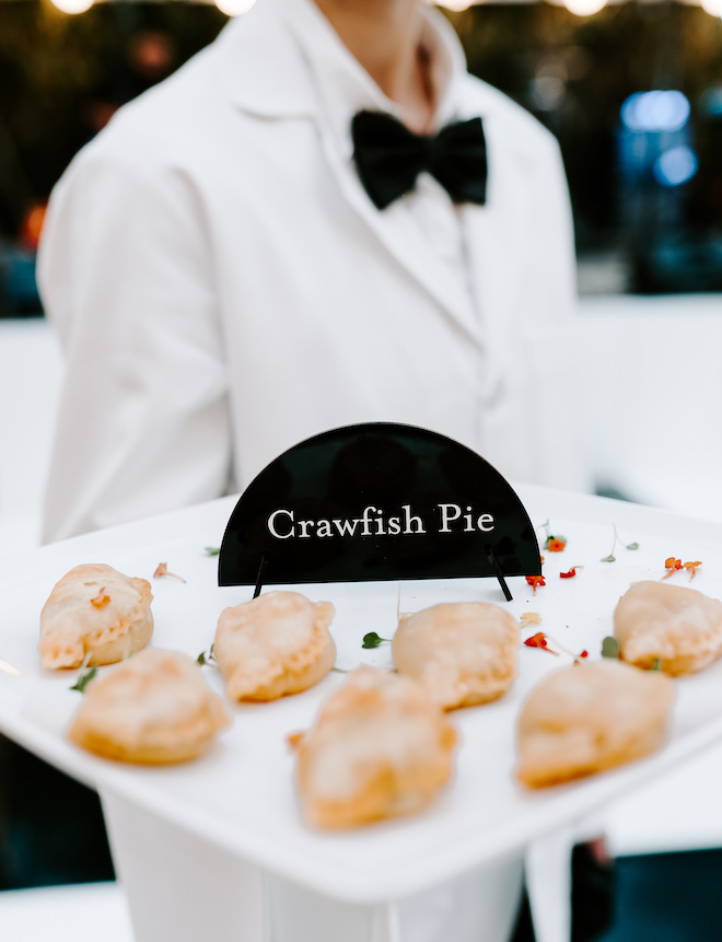 A waiter holding a tray of food with a "Crawfish Pie" sign.