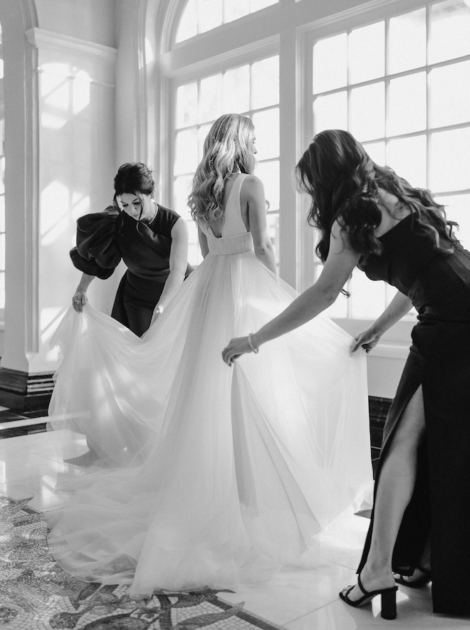 Two women helping the bride with her wedding dress.