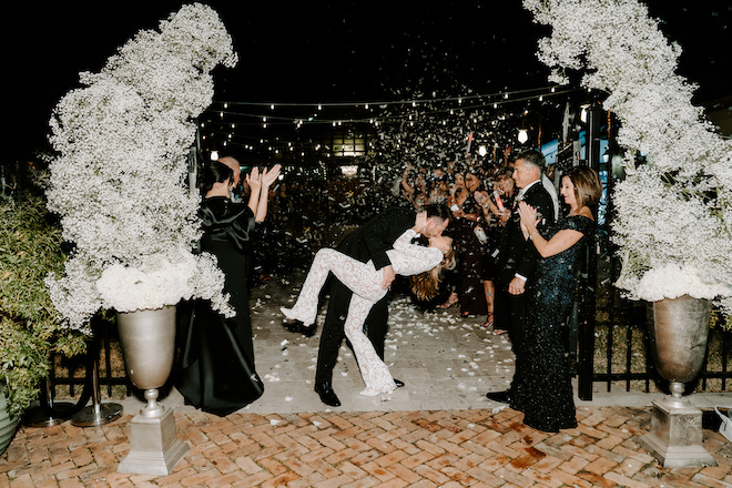 The bride and groom kissing as white rose petals are thrown in the air and guests clap at their winter wedding in Galveston, Texas.