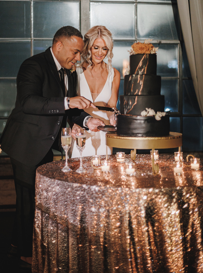The bride and groom cutting into their four-tier black and gold wedding cake.