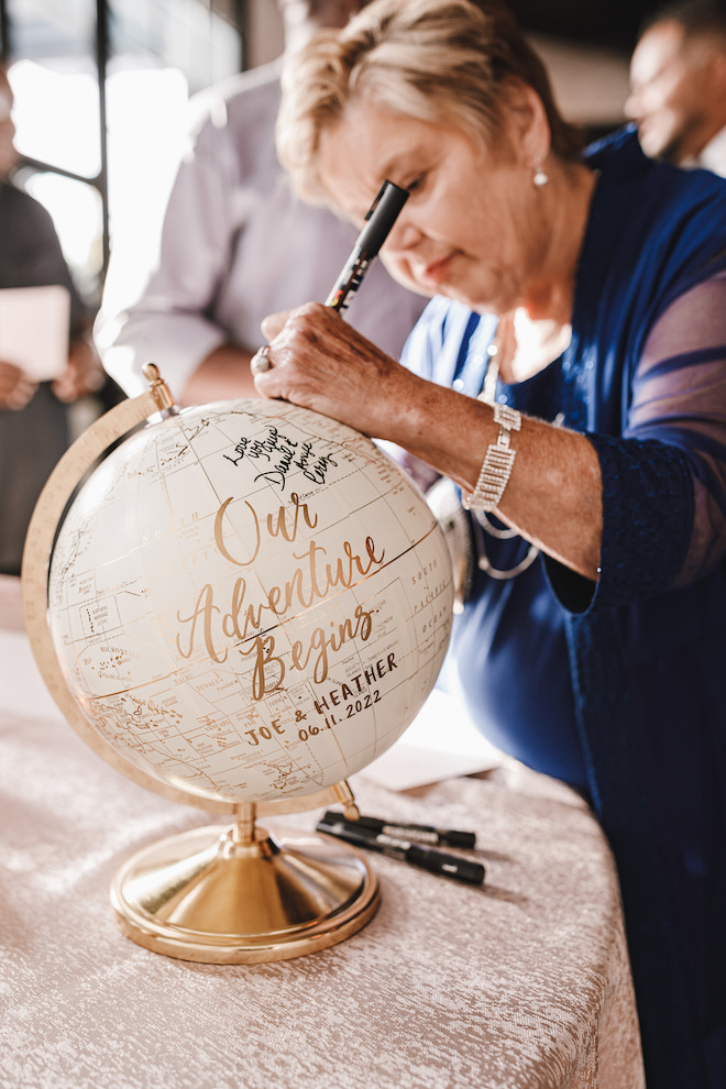 A woman writing on a gold and cream globe reading "Our Adventure Begins."