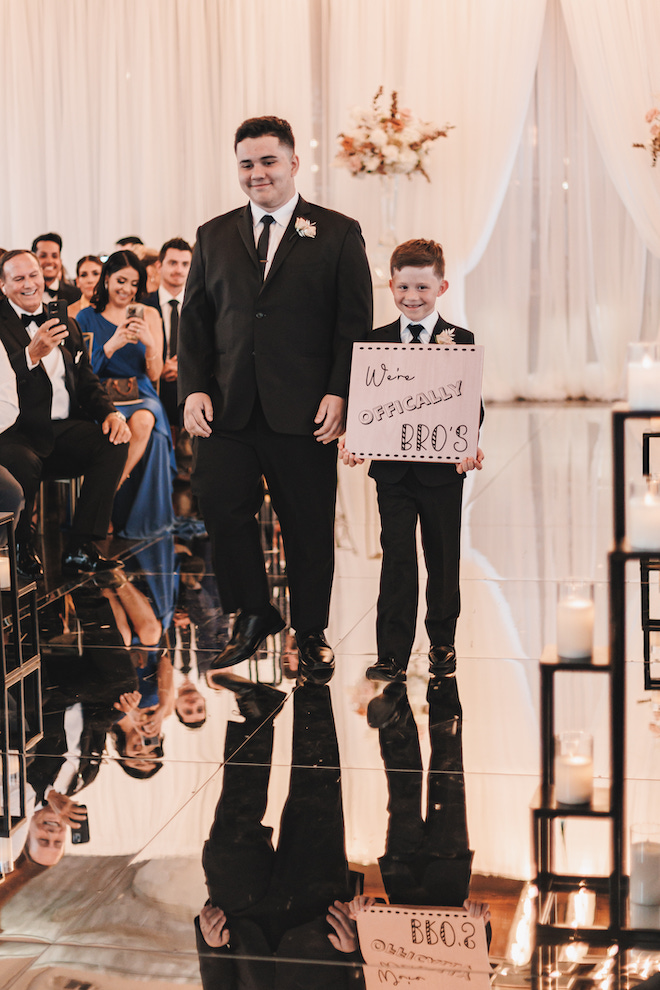 The bride and groom's sons walking down the aisle with a sign reading "We're officially bros."