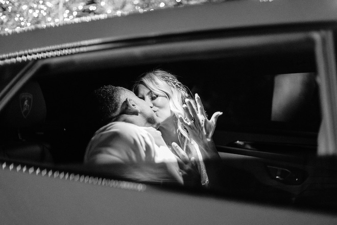 The bride and groom holding up their rings as they sit in the getaway car.